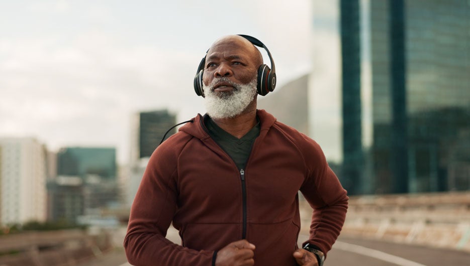 Mature, athlete and running in city with headphones for fitness, workout or marathon training music. Black man, thinking or exercise podcast in South Africa for cardio wellness, health or sport radio.